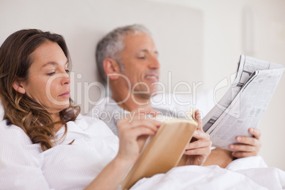 Woman reading a book while her husband is reading a newspaper