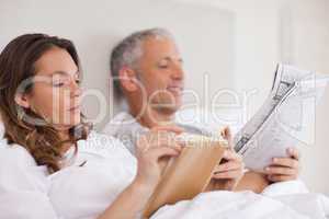 Woman reading a book while her husband is reading a newspaper