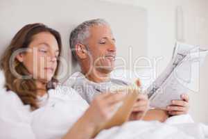 Happy woman reading a book while her husband is reading a newspa