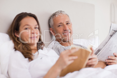 Happy woman reading a book while her husband is reading the news