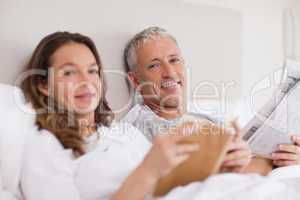 Happy woman reading a book while her husband is reading the news