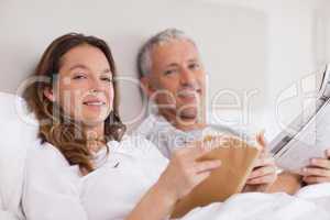 Smiling woman reading a book while her husband is reading the ne