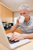 Portrait of a man using a laptop while drinking tea