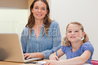 Girl doing her homework while her mother is using notebook