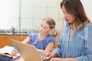 Little girl doing her homework while her mother is using noteboo