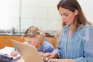 Little girl doing her homework while her mother is using laptop
