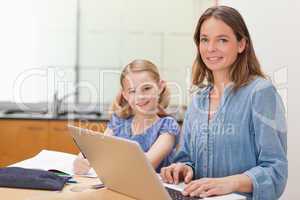 Girl doing her homework while her mother is working with laptop
