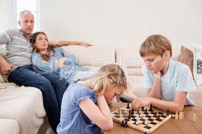 Children playing chess in front of their parents