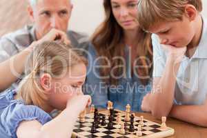 Focused children playing chess in front of their parents