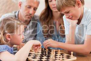 Close up of siblings playing chess in front of their parents