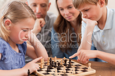 Close up of children playing chess in front of their parents