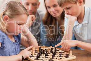 Close up of children playing chess in front of their parents