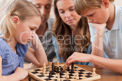 Close up of serious children playing chess in front of their par