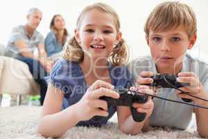 Playful siblings playing video games with their parents on the b