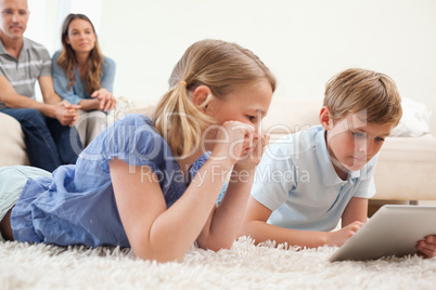 Children using a tablet computer with their parents on the backg
