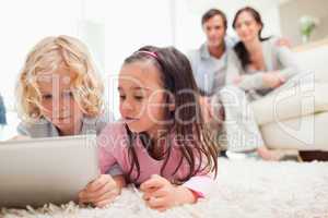 Cute siblings using a tablet computer while their parents are in