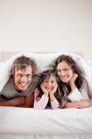 Portrait of parents lying under a duvet with their daughter