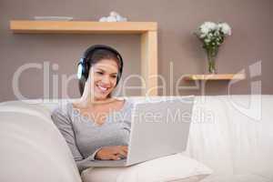 Smiling woman with headphones and laptop on the sofa