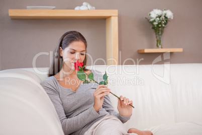 Woman on the sofa smelling on a red rose