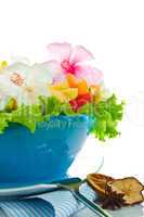 Fruit salad with edible flowers in a blue bowl from ice on white
