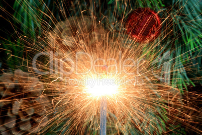 Burning (lit) sparkler in front of Christmas tree.
