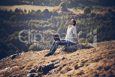 young man using laptop sitting on the grass on the hillside