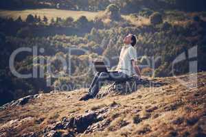 young man using laptop sitting on the grass on the hillside