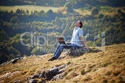 young man using laptop sitting on the grass on the hillside