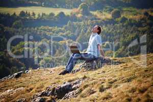 young man using laptop sitting on the grass on the hillside