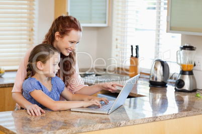 Mother and daughter with laptop behind the kitchen counter