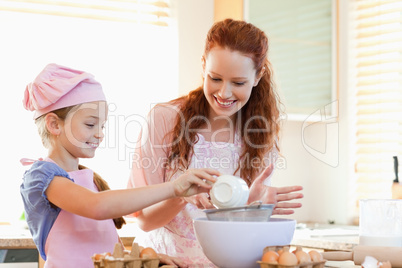 Smiling mother and daughter preparing dough