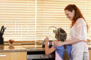 Cheerful mother showing her daughter how to cook