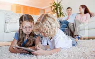 Siblings using tablet on the living room floor