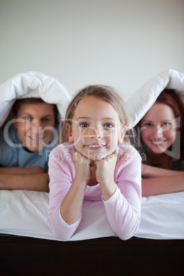 Smiling girl under bed cover with her parents