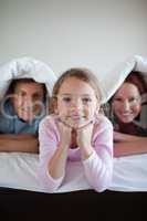 Smiling girl under bed cover with her parents