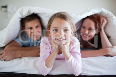 Cheerful girl under bed cover with parents