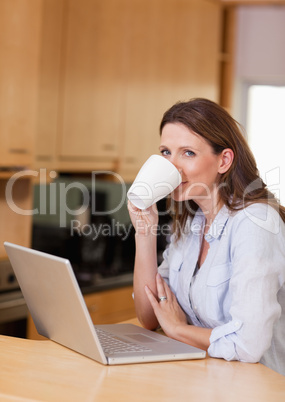 Woman taking a sip of coffee next to laptop