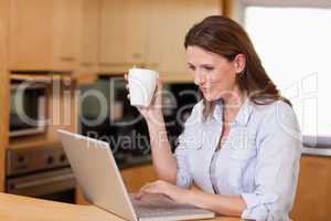 Woman drinking tea while on laptop