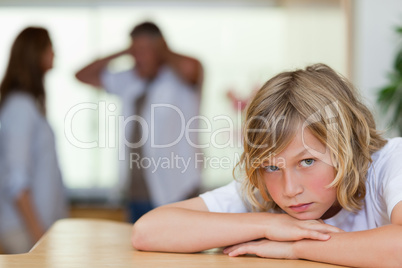 Sad looking boy with arguing parents behind him