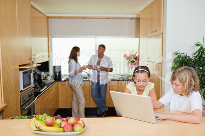 Children with laptop in the kitchen and parents behind them