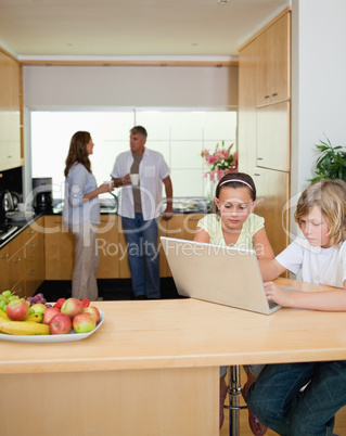 Siblings with notebook in the kitchen and parents behind them