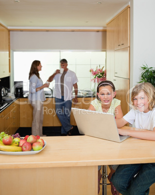 Siblings with laptop in the kitchen with parents behind them