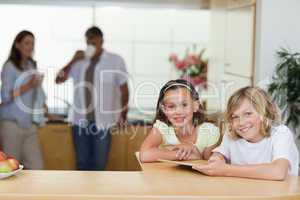 Siblings using tablet in the kitchen with parents behind them