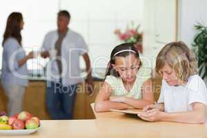 Children using tablet in the kitchen with parents behind them