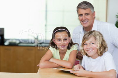 Smiling man with children and tablet in the kitchen