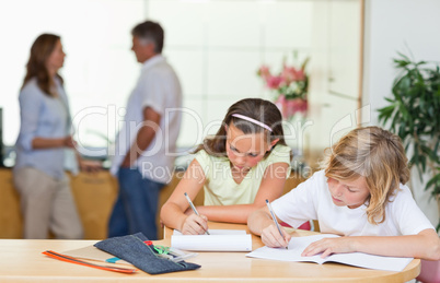 Siblings doing homework with parents behind them