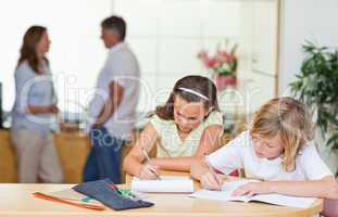 Siblings doing homework with parents behind them