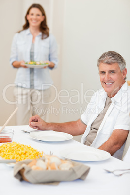 Man waiting for his wife to bring salad to the table