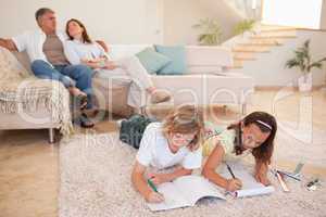 Siblings doing homework on the floor with parents behind them