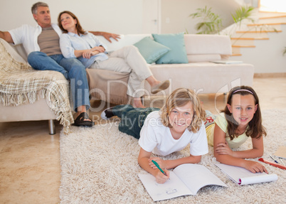 Siblings doing homework on the carpet with parents behind them